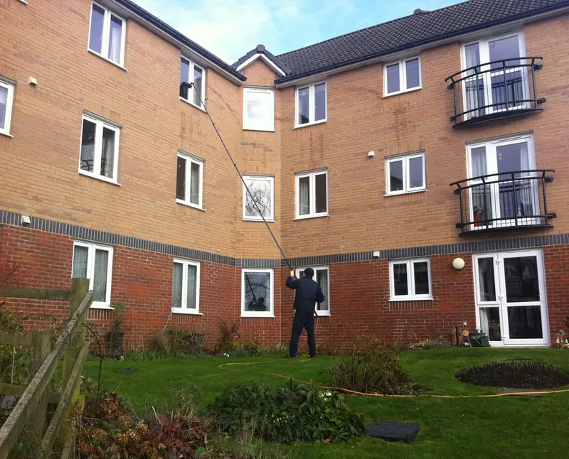 Window cleaner using a pole to clean the windows of a brick apartment block