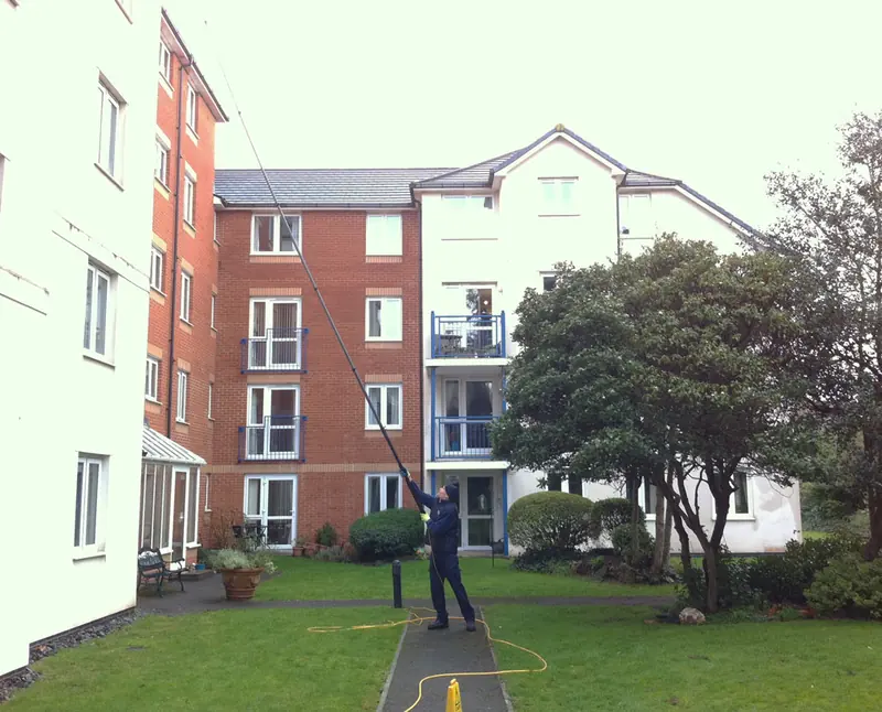 Window cleaner using a water-fed pole in the grounds of a residential block